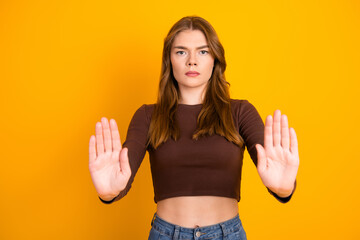 Young Woman Gesturing Stop with Her Hands Against a Vibrant Yellow Background as She Stands in...
