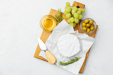Gourmet cheese platter with grapes, olives, honey, and rosemary on wooden board