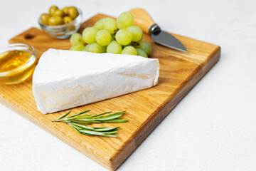 Cheese platter featuring brie, grapes, olives, and honey on wooden board