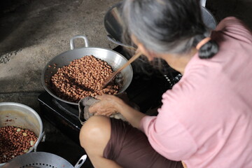 A grandmother is frying peanuts until they turn brown in a frying pan while sitting. The photo was...