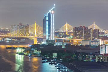 Aerial view of Bangkok city night light at Chao Phaya riverfront and bridge across the river with central business district.