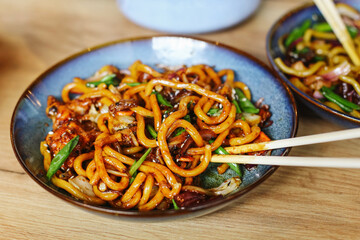 Asian noodles with vegetables. Udon stir fry on plate. Chopsticks on wooden table. Tasty Asian dish. Savory homemade meal. Colorful and spicy dinner. Fresh and hot traditional street food.