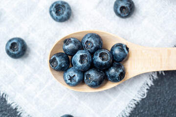 Fresh blueberries arranged on a wooden spoon against a textured background