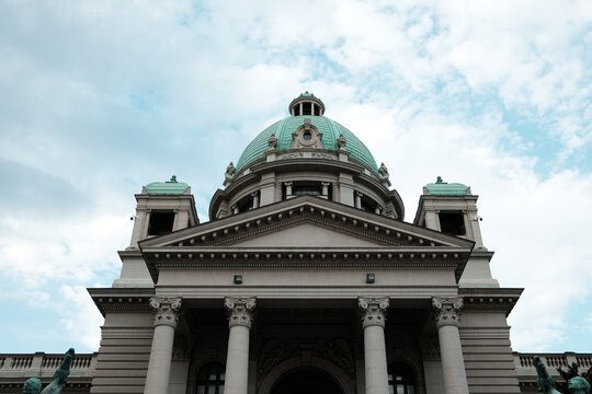 The National Assembly of the Republic of Serbia in Belgrade. A historic government building with green domes and neoclassical architecture under a cloudy sky.