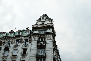Ornate historic building in Belgrade, Serbia. Decorative facade, balconies, and green roof tiles under a cloudy sky. Classic European architecture style.