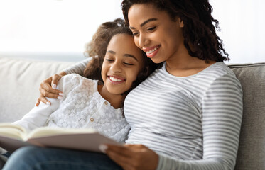 Fototapeta premium family lifestyle, leisure activity concept. Happy black mother and daughter reading book together at home, copy space. Beautiful african american family mom and child reading fairy tales