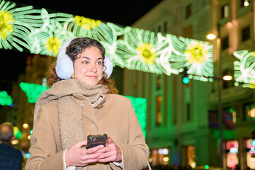 Young woman using smartphone under christmas lights in city center