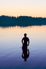 A man stands in a lake at sunset