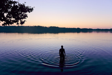 A man stands in a lake at sunset