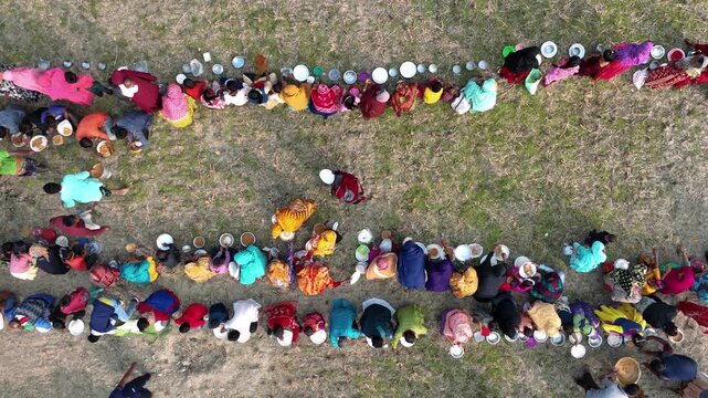 Bogura, Bangladesh - 25 July 2025: Aerial view of people sitting in rows on the grassy ground, eating from plates, a vibrant display of community and culture.