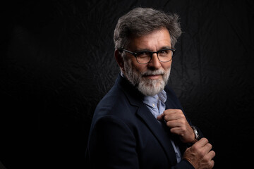 Mature handsome man looking at camera in studio with black background, elegant appearance and attitude