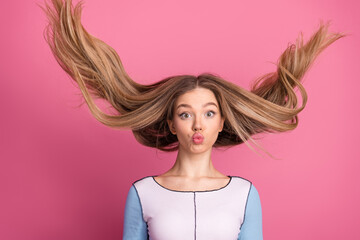 Cheerful young girl with flying hair making a funny expression on a pink background, showcasing vibrant charm and energy