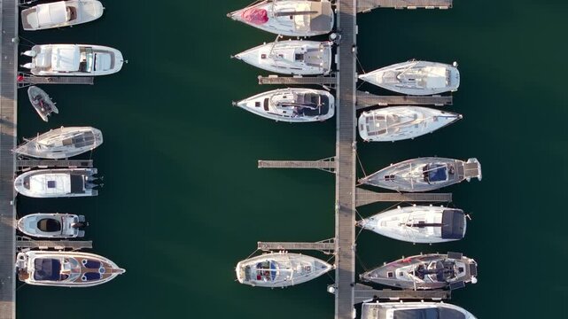Top-down aerial view of a marina at sunset, showing numerous yachts and boats neatly moored in parallel rows.