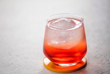 Closeup of a hand pouring sparkling water into a glass with red liquid and ice.