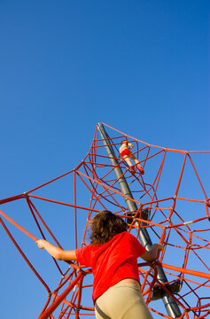 Red metal tower structure with a girl climbing under bright blue sky, capturing bold geometry and energy in abstract architectural urban space with dynamic upward composition.