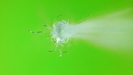 Close-up of gunshot through the glass, shattering against the green background