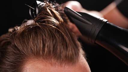 Young Man with Beard at Barber Shop. Barber is Preparing his Haircut. Dark Atmosphere, Black Background. Concept of Barber and a Client.