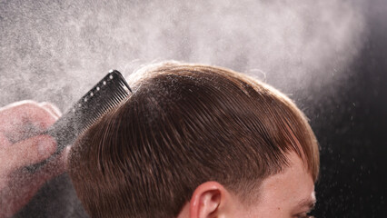 Young Man with Beard at Barber Shop. Barber is Preparing his Haircut. Dark Atmosphere, Black Background. Concept of Barber and a Client.