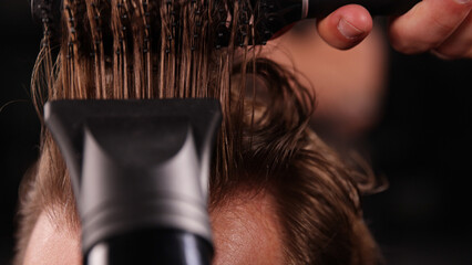 Young Man with Beard at Barber Shop. Barber is Preparing his Haircut. Dark Atmosphere, Black Background. Concept of Barber and a Client.