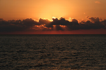 Naklejka premium Beautiful sunset over the sea. The rays of the sun break through the clouds. Sunset over the sea with clouds and rays of the sun.