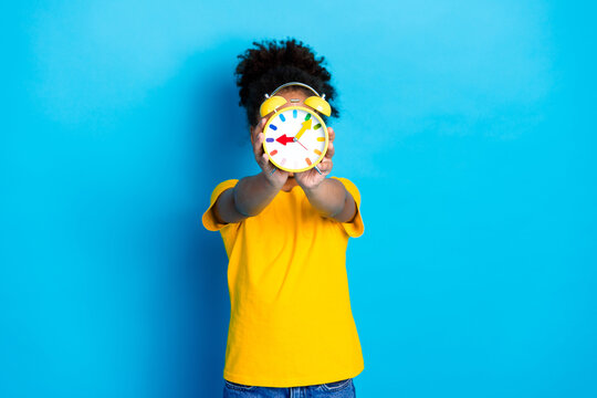Cheerful young girl holding a colorful alarm clock against a vibrant blue background, emphasizing punctuality and creativity - Powered by Adobe