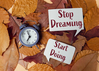 Alarm clock on autumn leaves with motivational quotes encouraging action and productivity