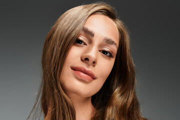 Fototapeta premium Young beautiful woman gazes confidently with soft waves of hair in a neutral backdrop