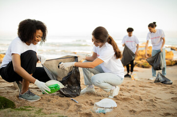 Positive young different people volunteers in gloves with garbage bags clean up trash on sea beach, outdoor. Ocean pollution and environment conservation, protecting planet, Earth day