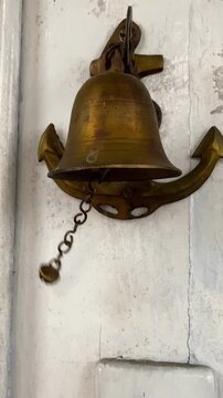 The vintage copper bell is softly swaying on the hung white wooden door. Captured in a slow state, the scene causes nostalgia and timeless charm. Ideal for visual effects of travel or heritage.