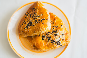 Two golden flaky pastries are placed on a white plate topped with black sesame seeds The lighting suggests a bright afternoon creating an appetizing atmosphere