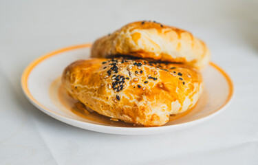 Two golden flaky pastries are placed on a white plate topped with black sesame seeds The lighting suggests a bright afternoon creating an appetizing atmosphere