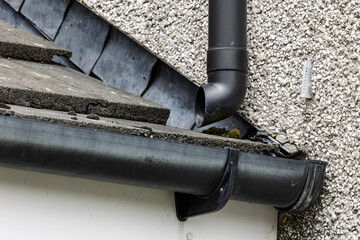 Black plastic rain downpipe and guttering on exterior wall of house © Tosh Lubek