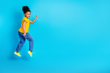 Fototapeta premium Happy young girl jumping playfully in vibrant yellow top against bright blue background showcasing energy and joy