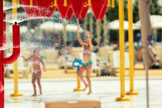 Two youthful figures in swimwear are experiencing the refreshing cascade of water at a vibrant water park. Water splashes abound, creating a playful and cooling summer environment