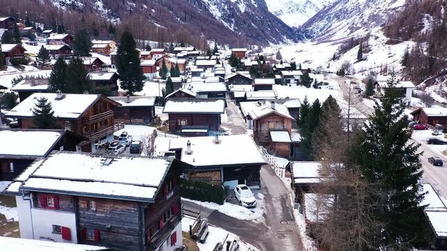 Aerial view of Zinal village nestled amid snow-covered roofs and mountains, a stark contrast against the dark trees, Anniviers, Valais, Switzerland.