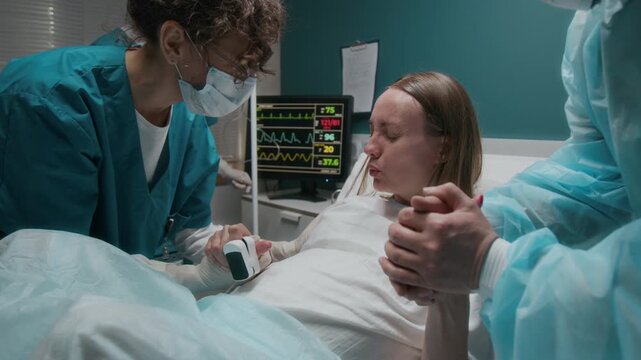 Medium close-up of sweaty pregnant Caucasian woman breathing in rhythm, screaming pushing during labor contractions, while giving birth to baby in maternity hospital, with husband and midwife