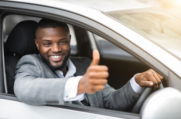 Side view of african american businessman in suit driving expensice car, smiling happily and...
