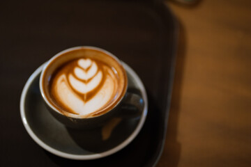 A cup of coffee on black tray with beautiful latte art at cafe from above.