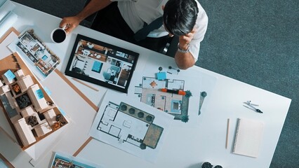 Top view of engineer drink coffee and thinking about house plan at meeting table with equipment and safety helmet scatter around. Aerial view of stressful manager looking at blueprint. Alimentation.