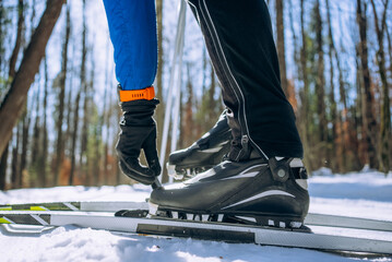 Close-up view of a skier fastening cross-country ski boots onto skis while surrounded by a snowy forest, getting ready for an exhilarating winter sports adventure