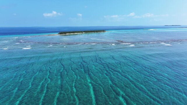 Aerial view of a tranquil island with dense trees surrounded by vibrant turquoise waters and gentle waves, Naavaidhoo, Haa Dhaalu City, Maldives.