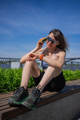 Fit athlete resting on bench, scrolling smartphone and monitoring fitness data after high-intensity training during warm summer afternoon, experiencing post-workout recovery moment