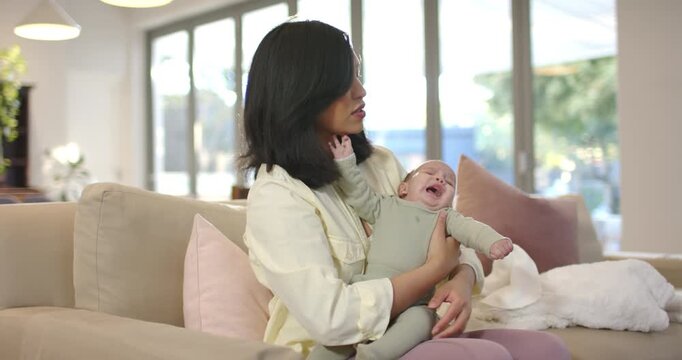 Mid adult woman responding to infant fussing, rocking baby on sofa at home to calm child