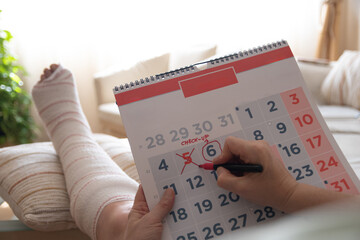 Patient resting with injured leg wrapped in plaster cast marking medical check-up appointment date on calendar, highlighting importance of timely healthcare management