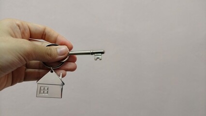 Hand holding a silver key with house shape keychain. Housing and property investment concept. House key.