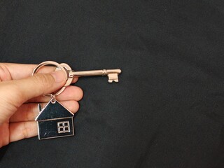 Hand holding a silver key with house shape keychain. Housing and property investment concept. House key.