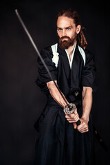 Samurai warrior in traditional Japanese clothing holding a katana sword in a dramatic pose on a dark studio background. Concept of martial arts, Japanese culture, and ancient warriors.
