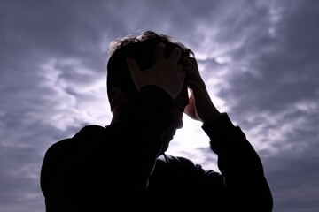 Silhouette of young adult male under moody cloudy sky