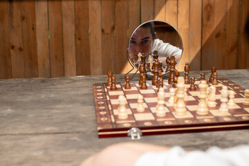 Chessboard with a chess pieces and face of a young woman reflected in a mirror	