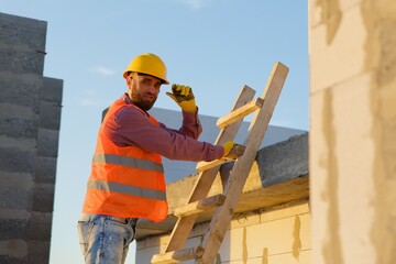 Construction worker inspecting building on ladder at sunset
